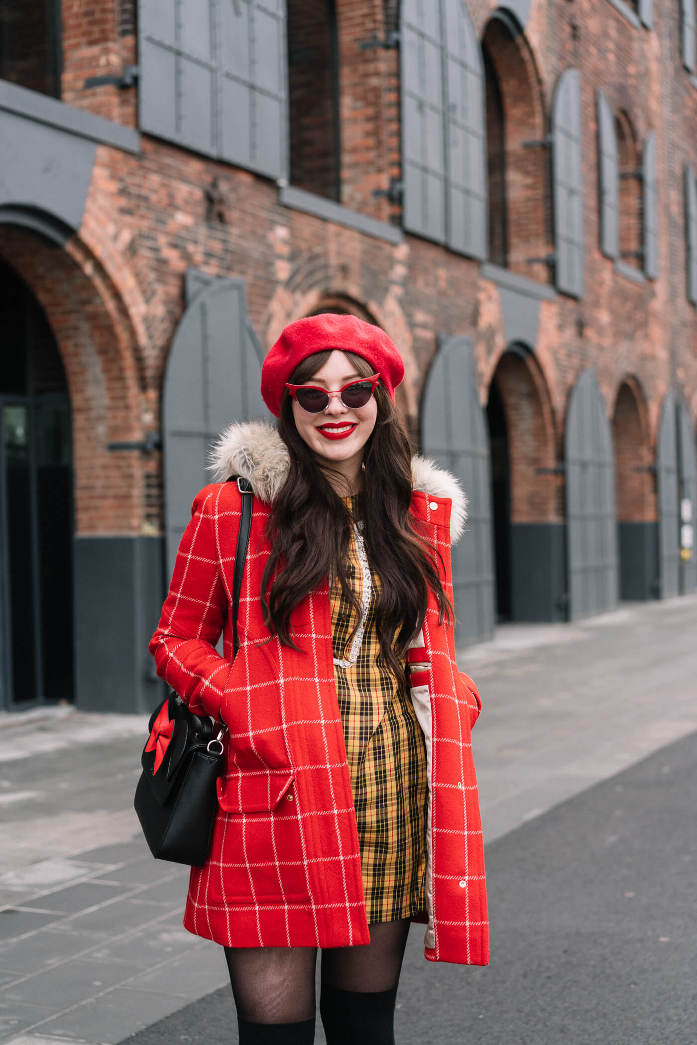 Keiko Lynn wearing a red checkered parka, vintage yellow plaid dress, red beret, minnie mouse bag, betty and veronica sunglasses, and black suede strappy block heels