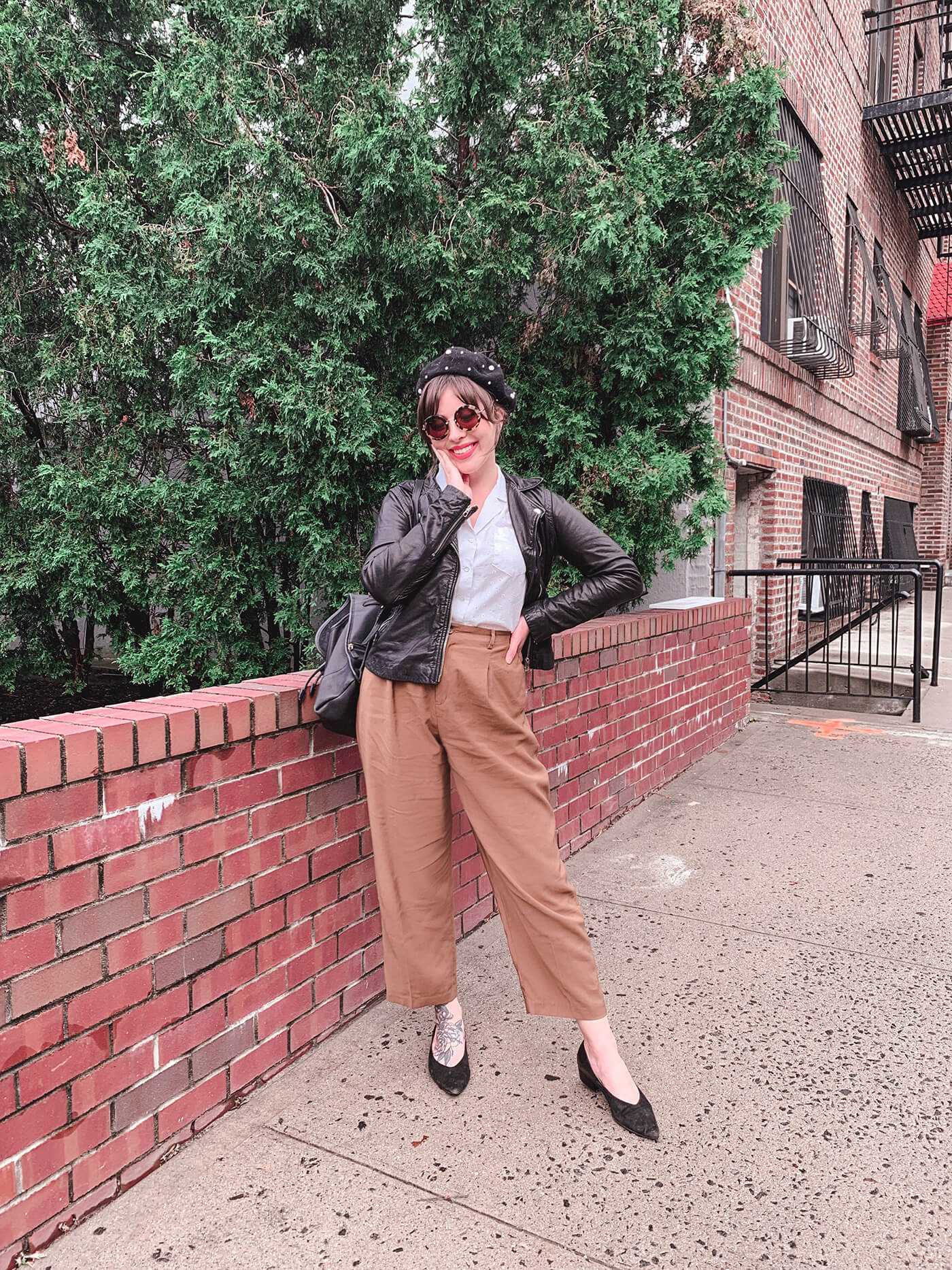 woman in white top, black leather jacket, and brown pants