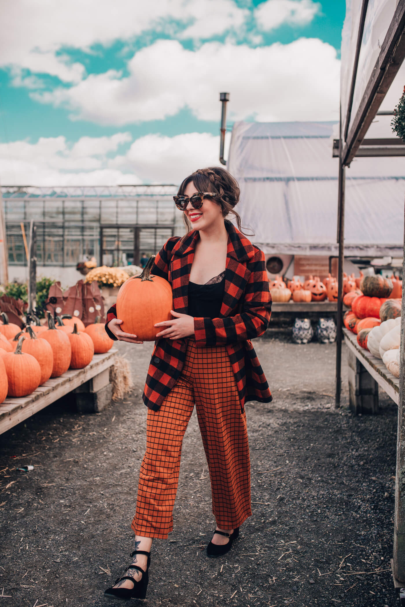 woman wearing plaid pants, black top, and plaid sweater and holding a pumpkin 