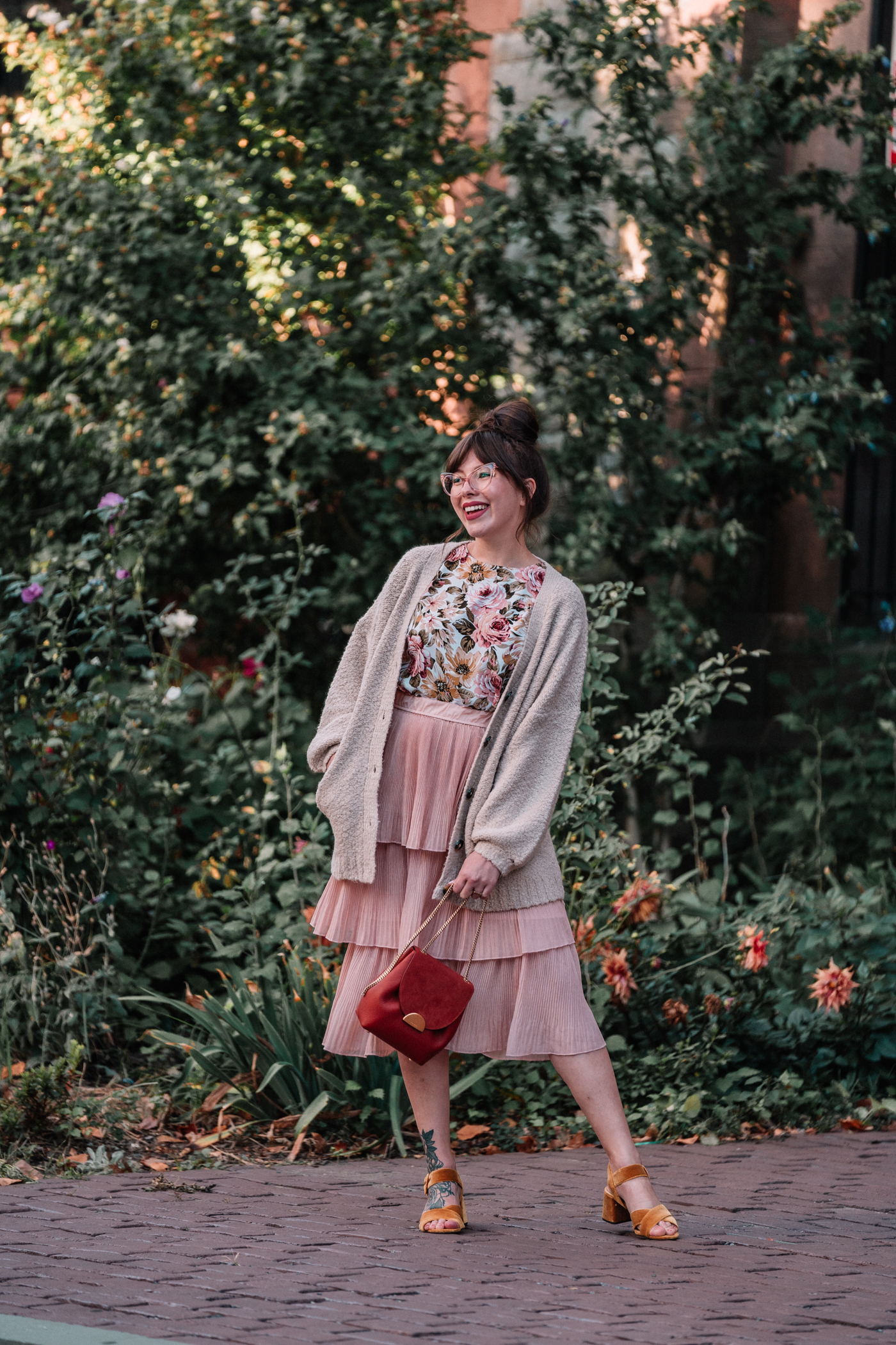 woman smiling and wearing floral fall outfit with tiered blush skirt, cozy knit sweater, and velvet heels for Go forward with kindness