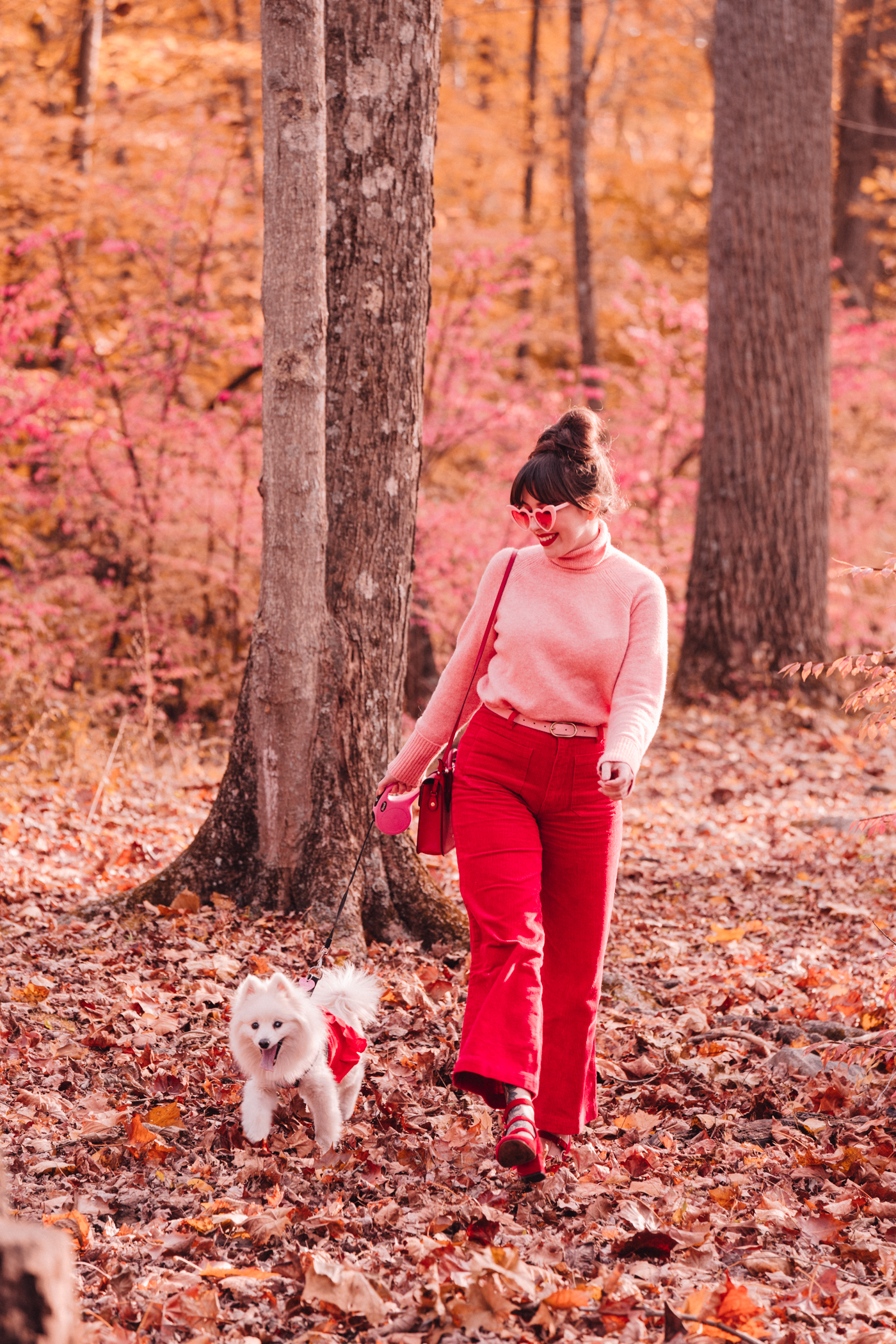 woman smiling and wearing pink and red top and pants in the outdoors with her dog