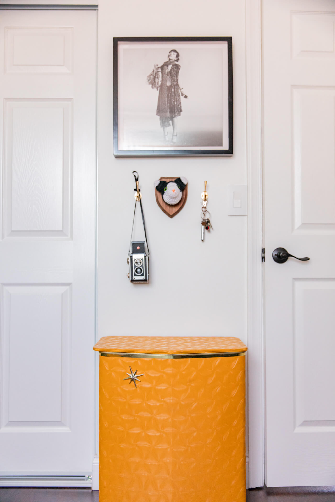 two closed doors, hanging vintage camera, keys, a painting and a yellow storage for HomeGoods Home Office Makeover