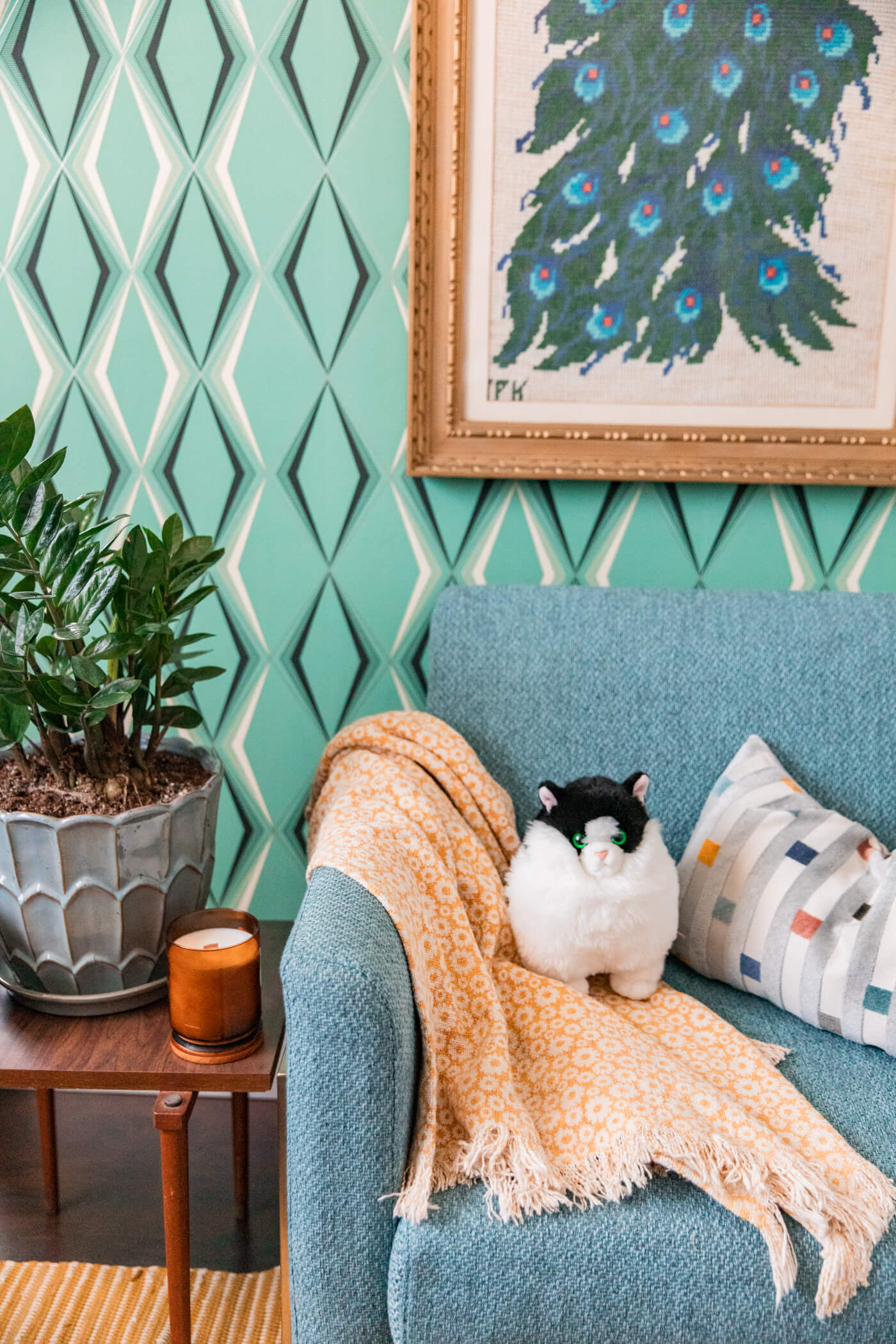 blanket and pillow on blue chair, indoor plants and candle on a corner table, and a hanging painting 