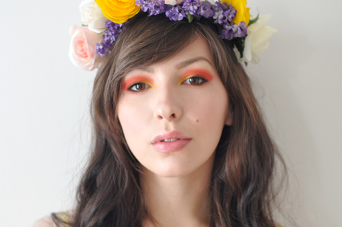face of a woman wearing orange signature eye makeup and a floral head dress