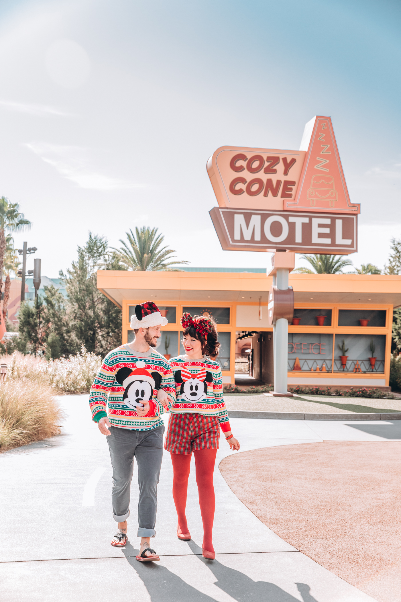 couple wearing holiday disney outfit and walking outside the cozy cone motel 