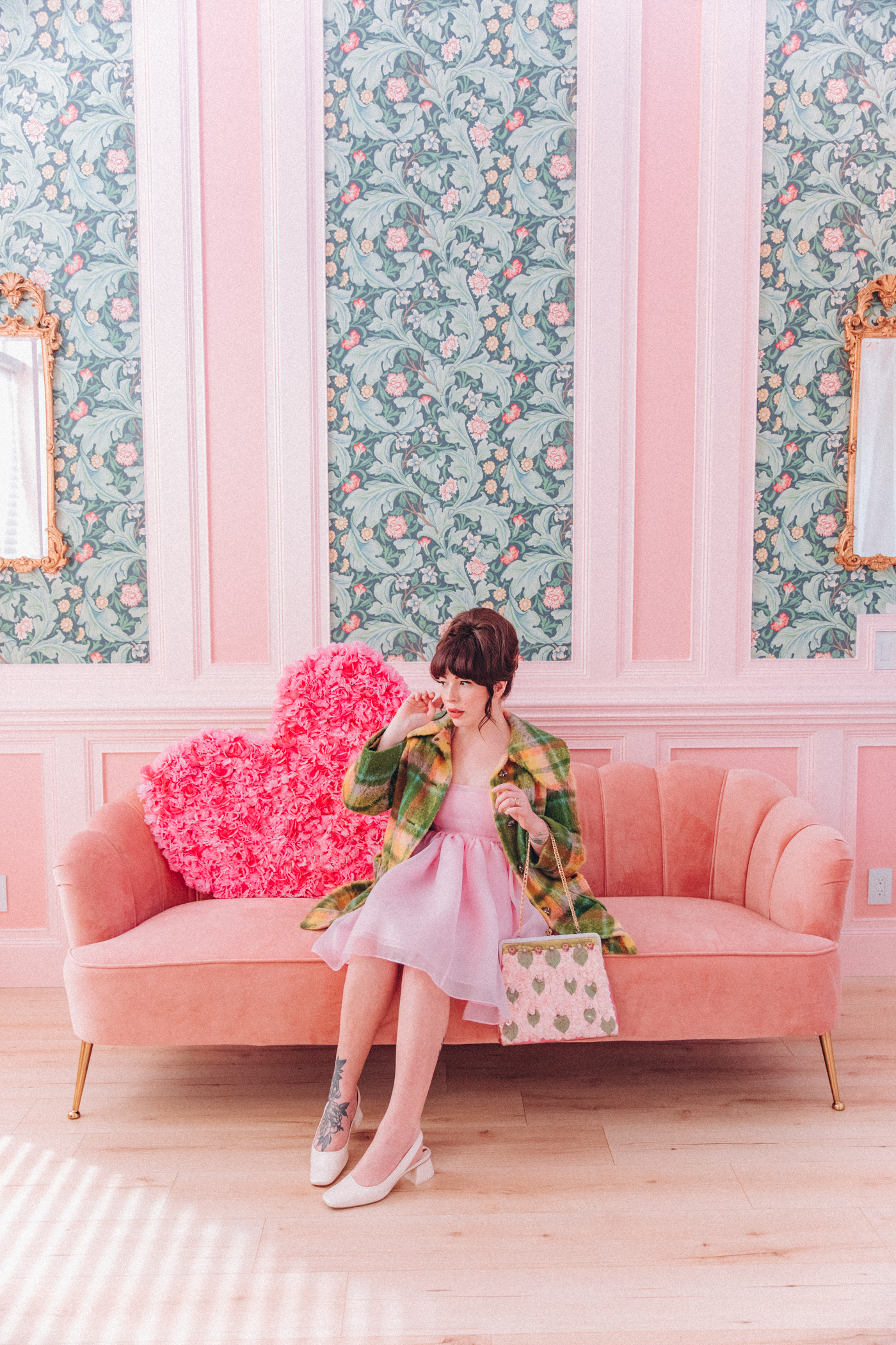 woman sitting on a pink couch and wearing coat and dress with her most worn shoes