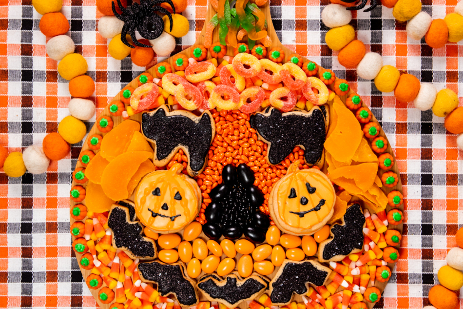 wooden snack board with assorted orange and black snacks assembled to resemble a pumpkin