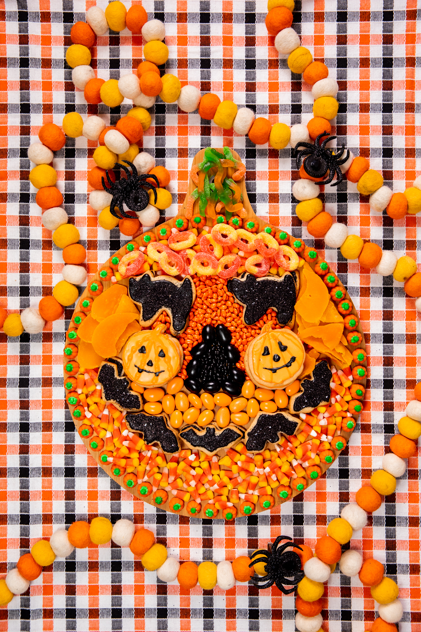 wooden snack board with assorted orange and black snacks assembled to resemble a pumpkin