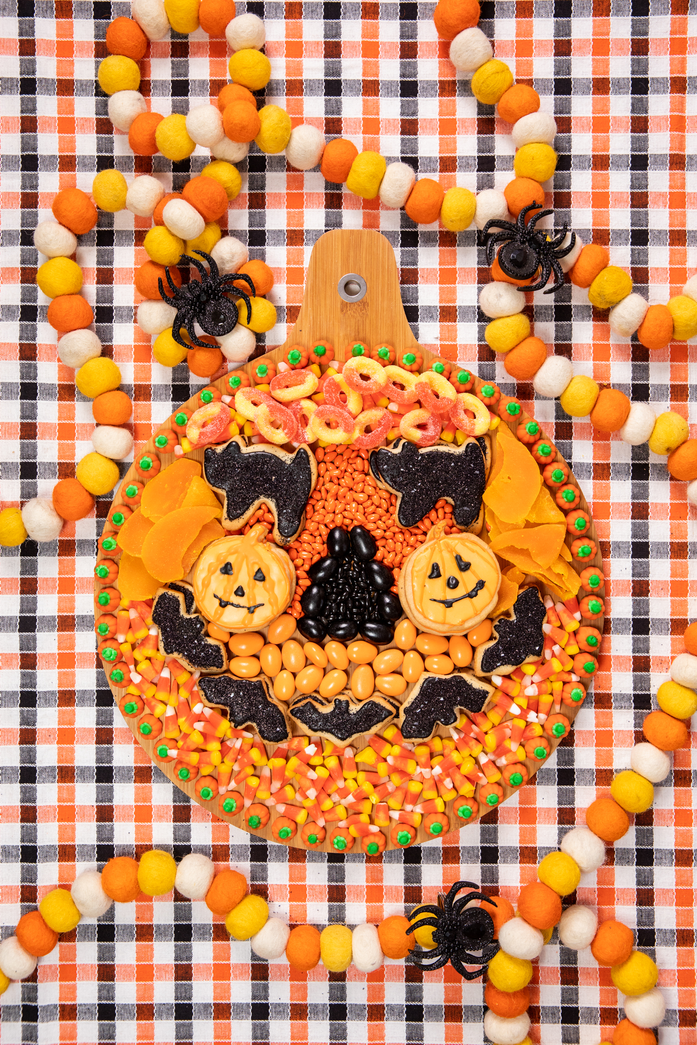 wooden halloween snack board with assorted orange and black snacks assembled to resemble a pumpkin