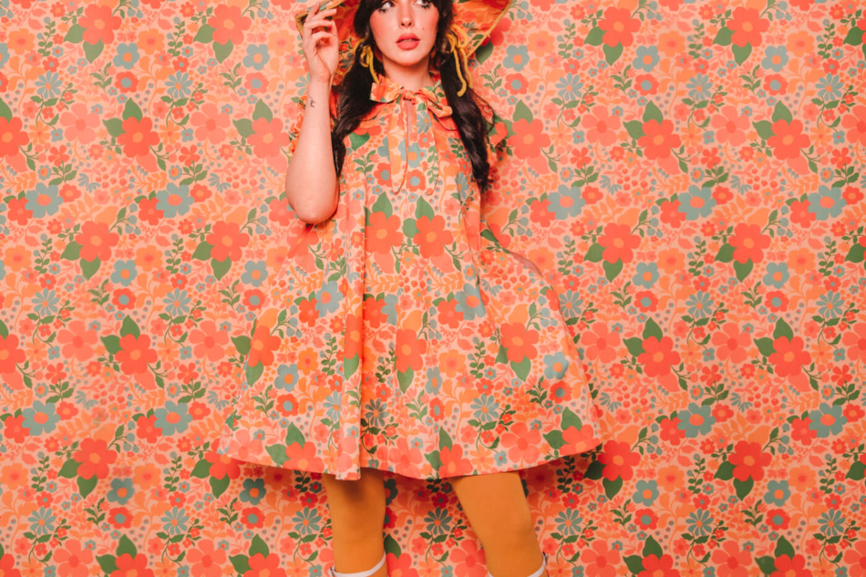 Keiko Lynn wearing a handmade dress and matching witch hat made out of Spoonflower fabric, in front of matching wallpaper in the same print.