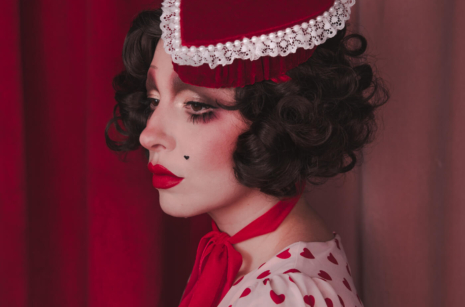Pale girl with dark 20s 30s style hair and makeup, wearing a red velvet heart shaped box hat